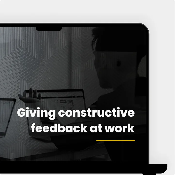 A laptop showing a dark module cover: “Giving constructive feedback at work”.